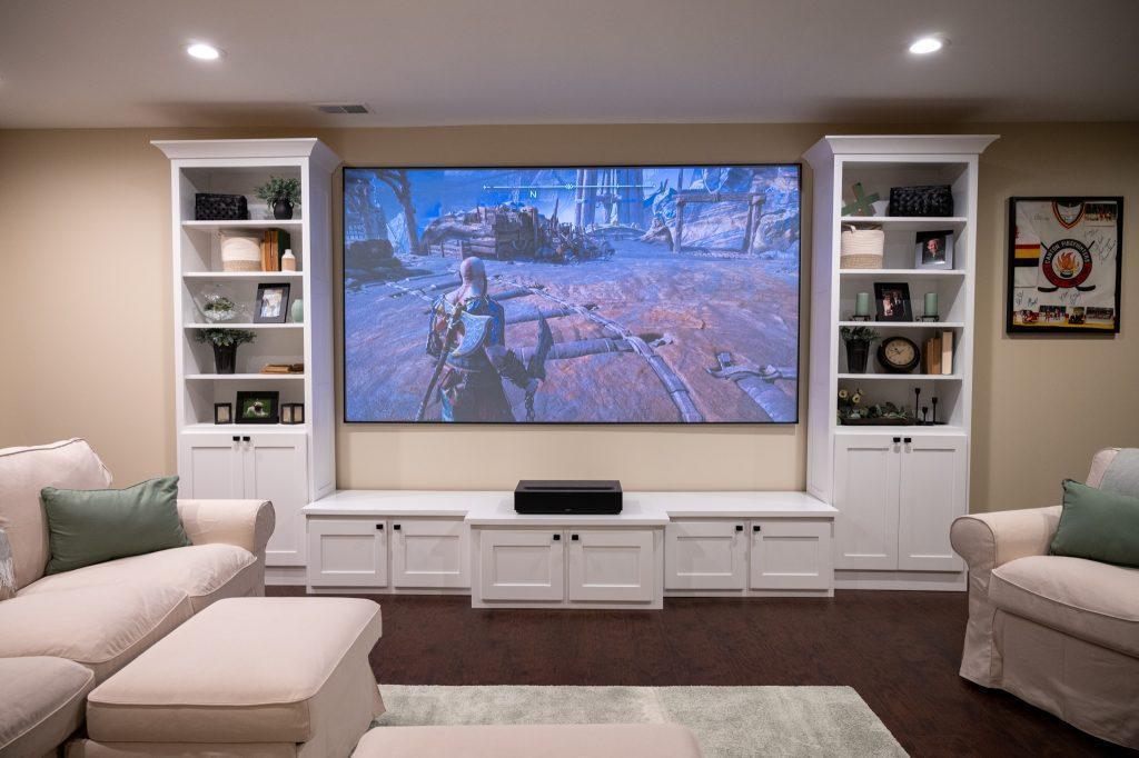Finished basement living room with large projection screen and shelving to display books, photos and music.
