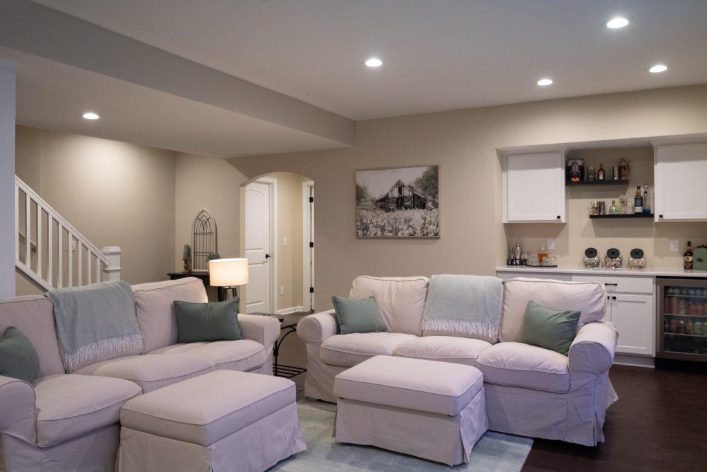 Finished basement living room area with dry bar in the background with spirits and snacks for watching movies.