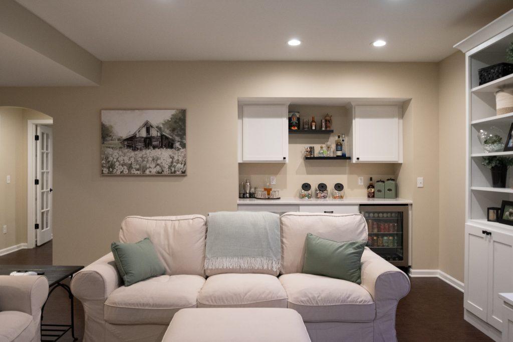Finished basement living room area with dry bar in the background with spirits and snacks for watching movies.