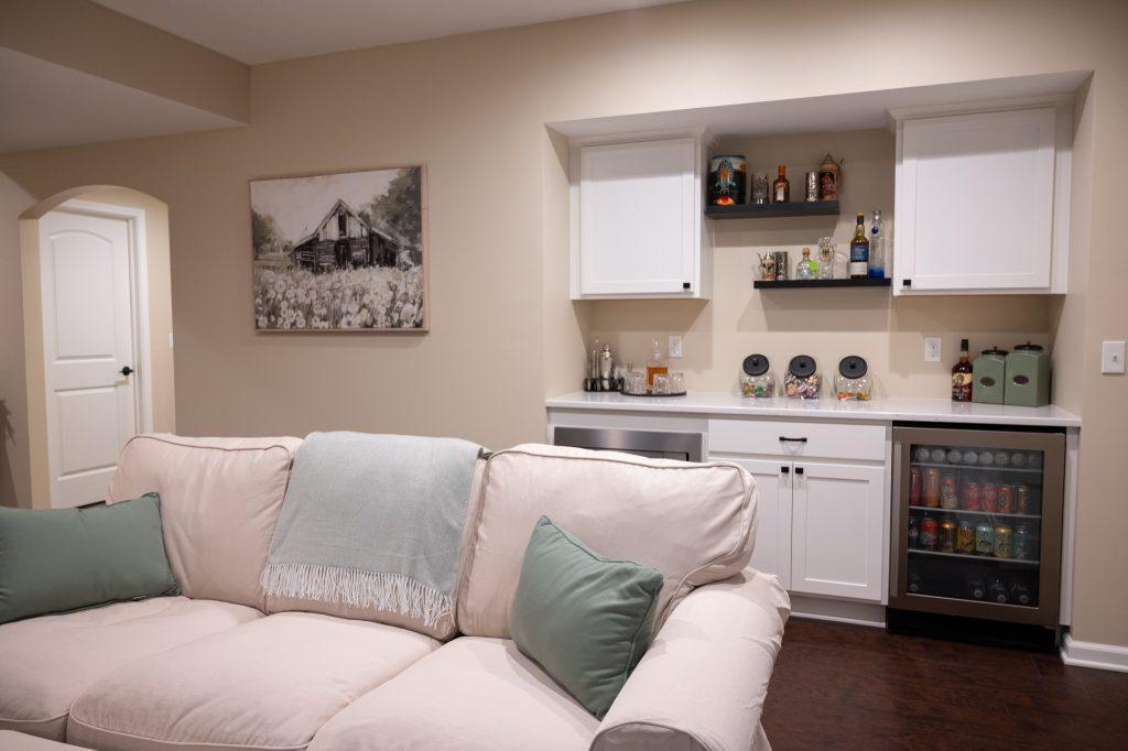 Finished basement living room area with dry bar in the background with spirits and snacks for watching movies.