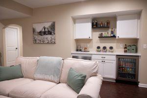 Finished basement living room area with dry bar in the background with spirits and snacks for watching movies.