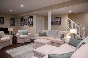 Finished basement living room with the stairs and storage access in the background.