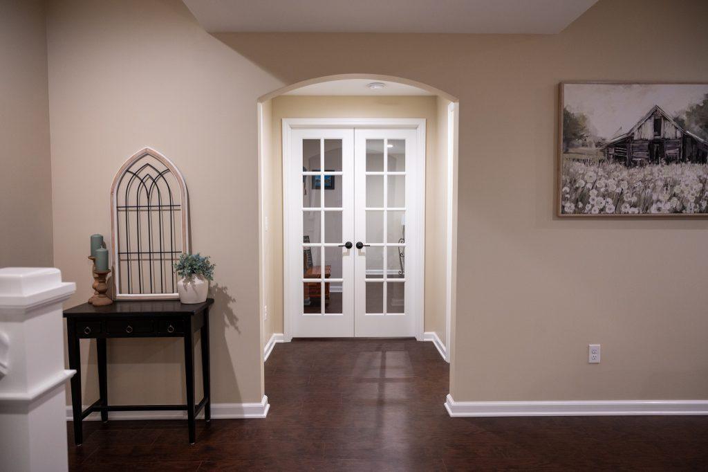 Finished basement looking down the hallway into a double door entrance to the guest room.