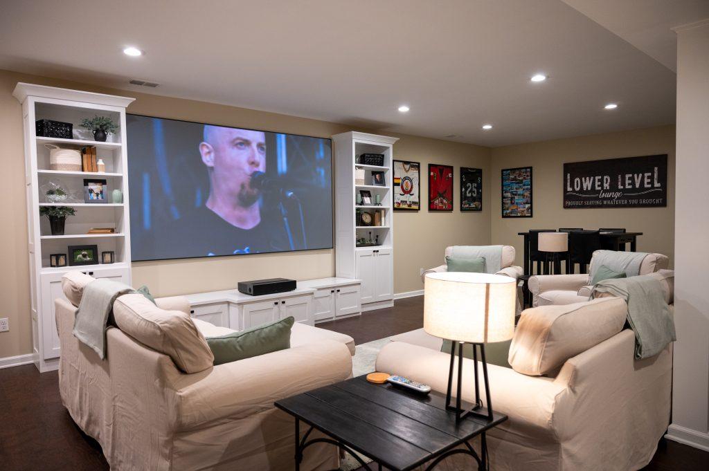 Finished basement living room view from bottom of the stairs towards the sitting area and projection screen.
