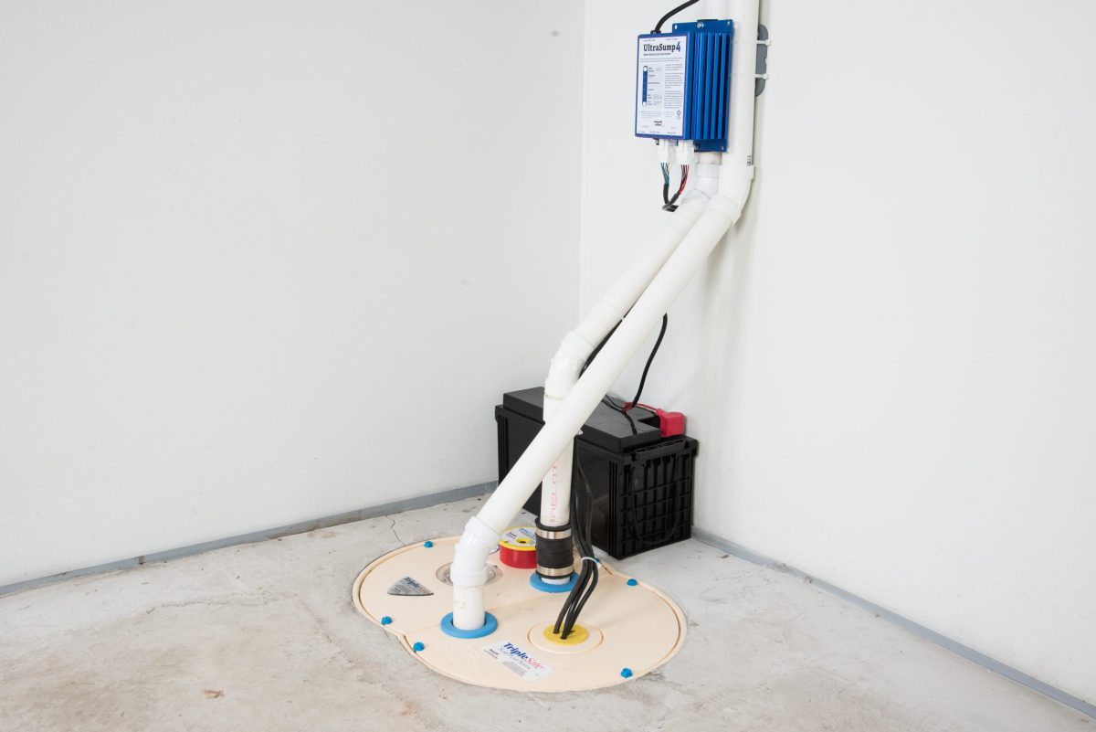 TripleSafe sump pump installation by Basements Plus. White PVC pipes running from a basin with battery backup.