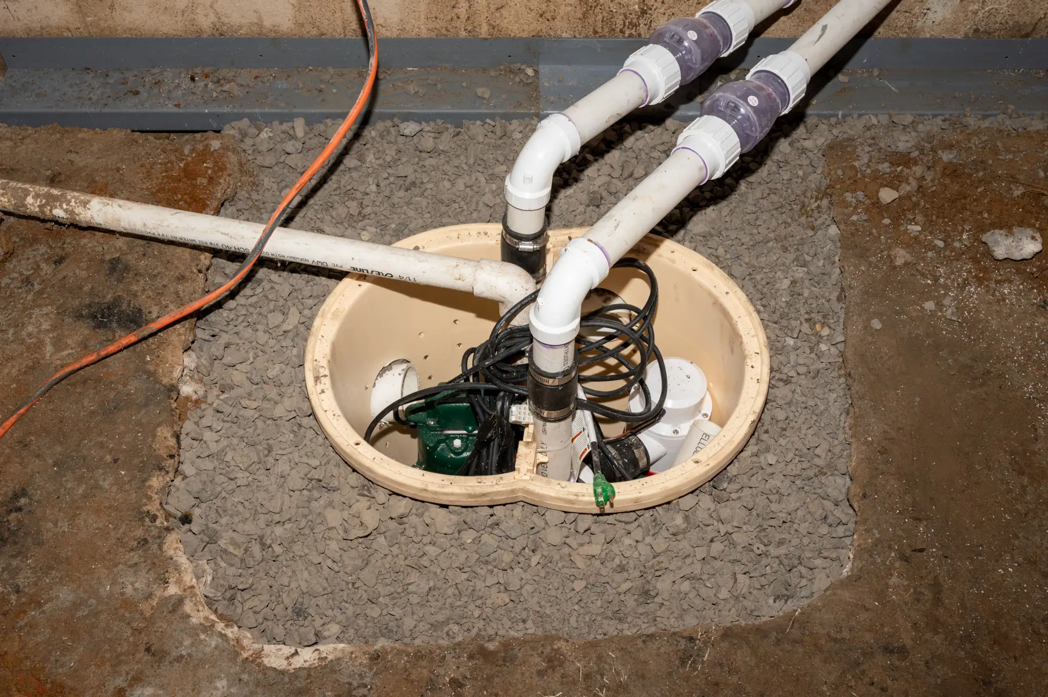 Photo of green sump pumps installed in a basin by Basements Plus crew members.